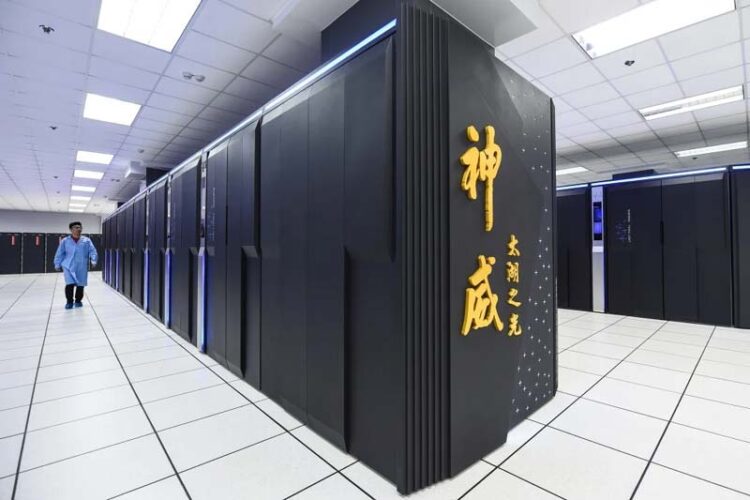 O supercomputador militar chinês Tianhe em uma sala de piso branco. Ao lado da máquina um homem caminha em direção à câmera. Parece ser um nacional da China. Ele usa jaleco azul.